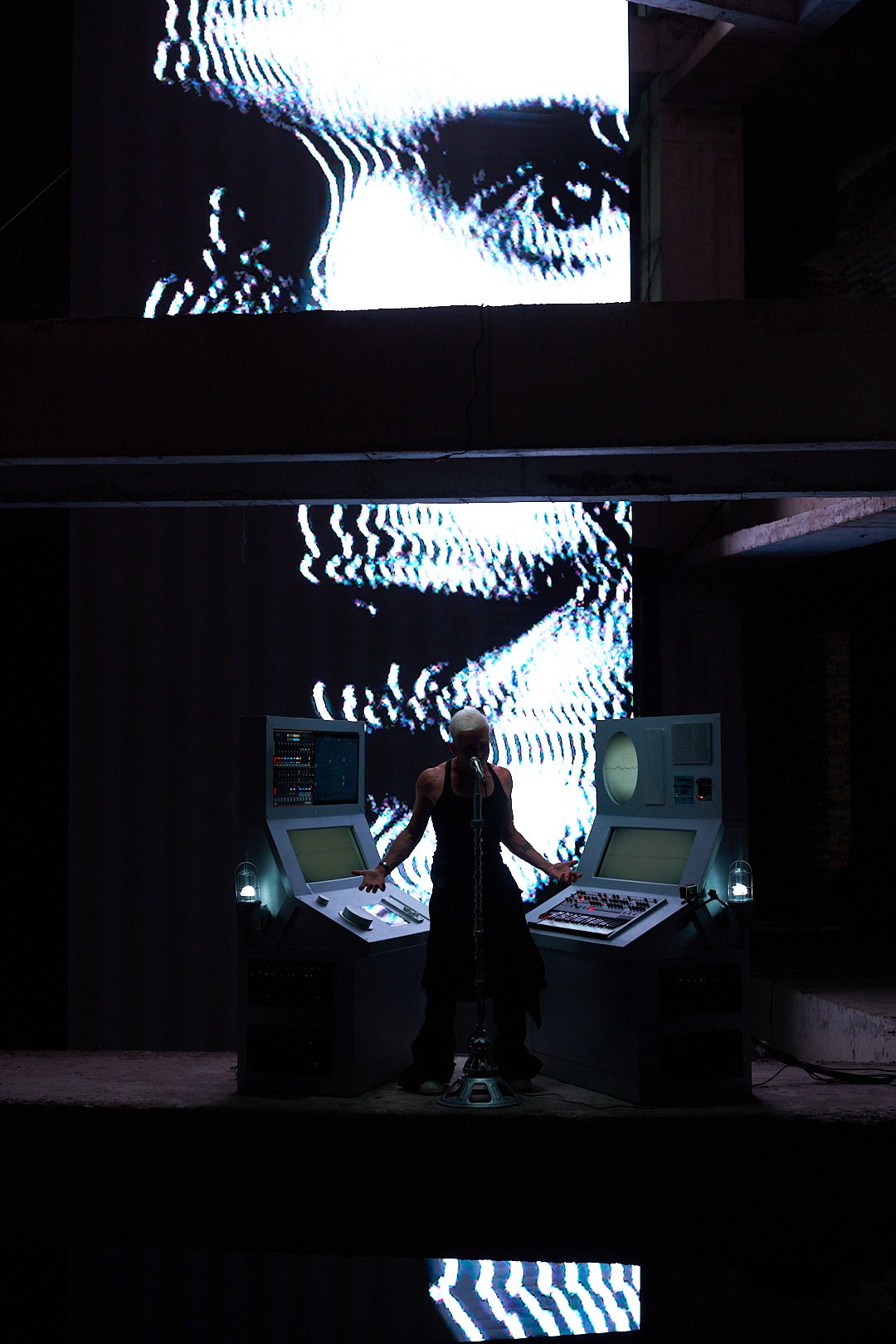 M07 performing between custom consoles and large projected faces in a concrete building in Hanoi