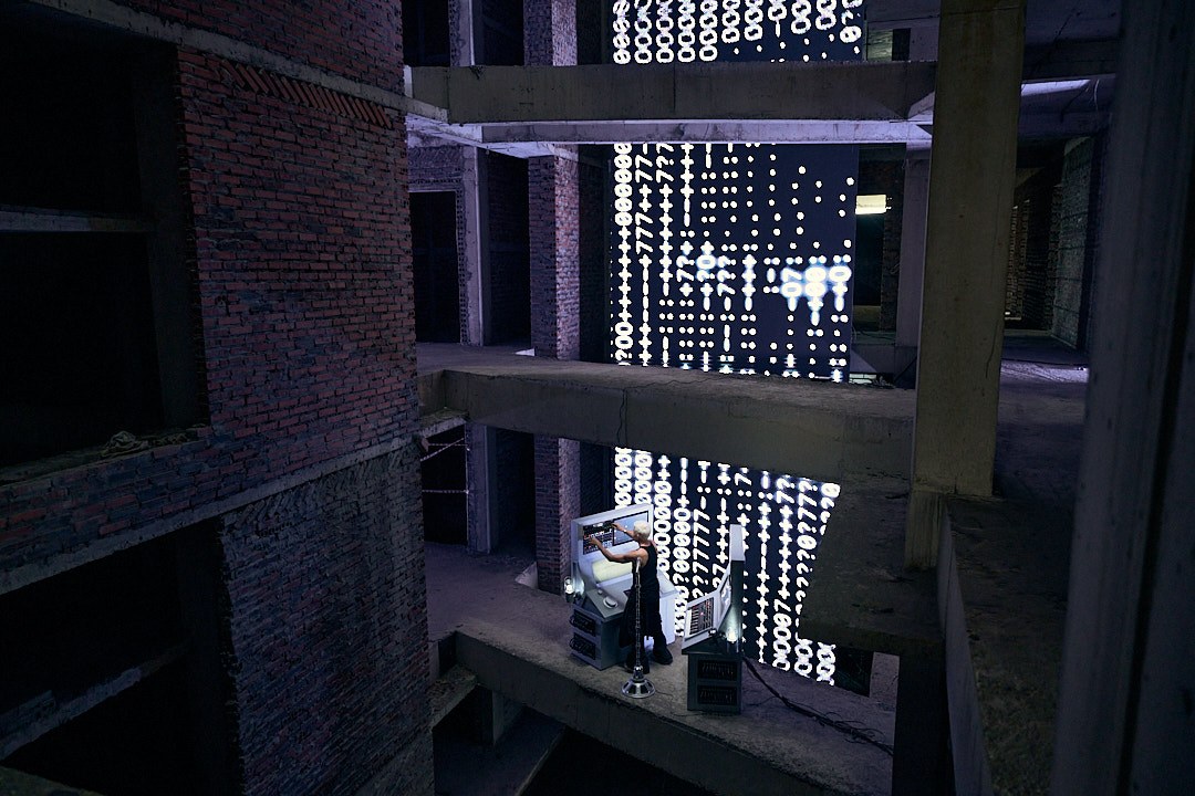 M07 and the custom instruments framed by multiple concrete floors and a tall illuminated screen in Hanoi