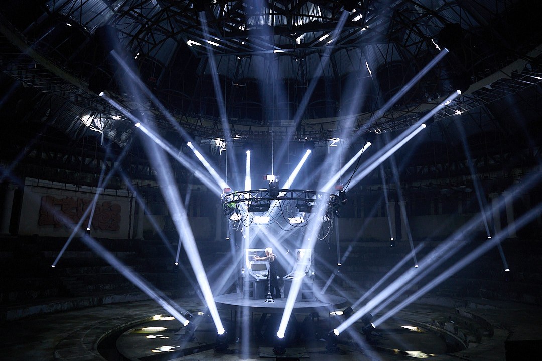 A wide view of white light beams radiating around M07 and the live platform inside the circus